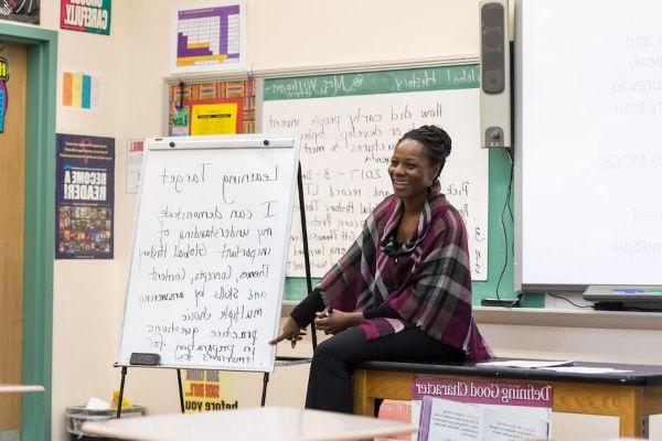 A teacher laughing at 的 front of a classroom, discussing learning targets with her students