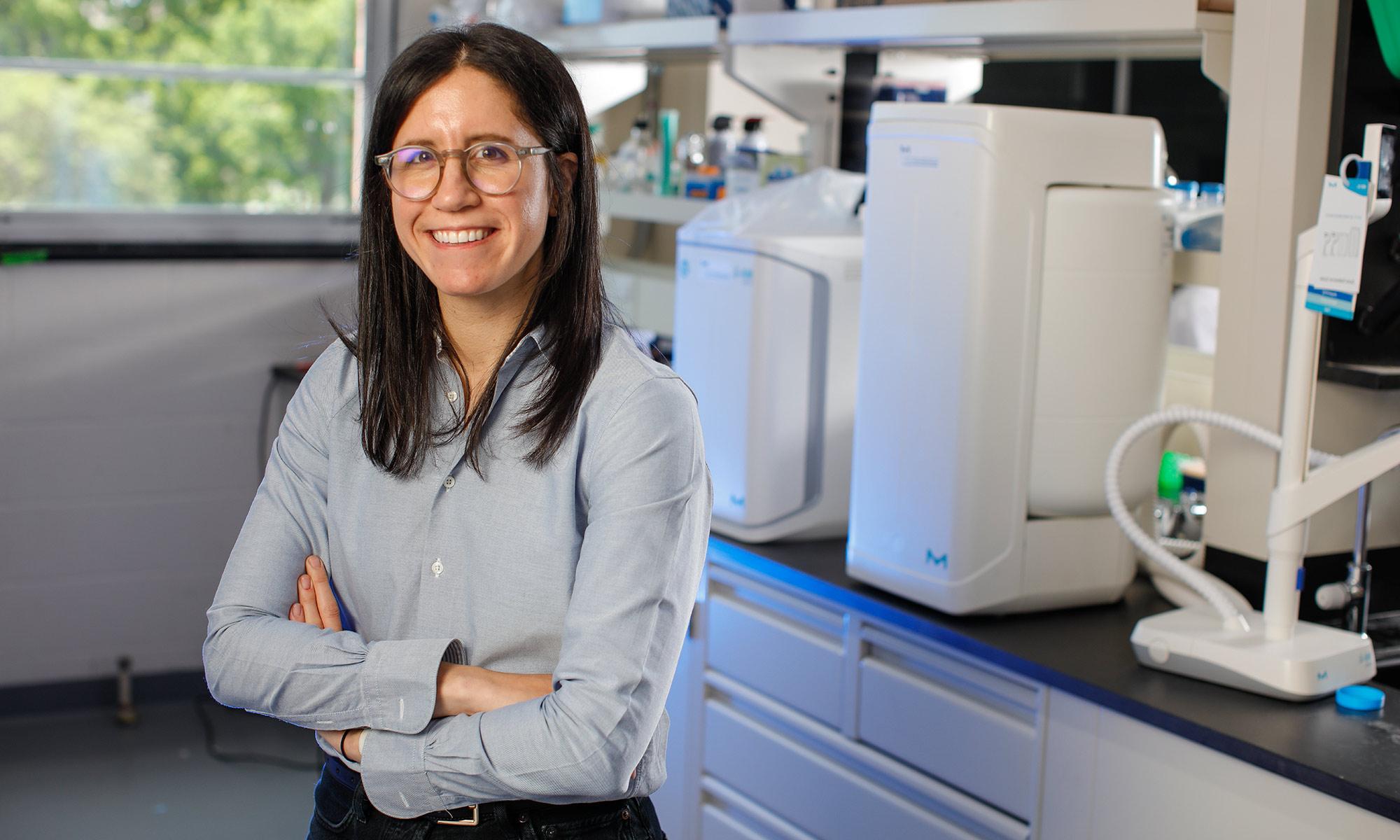 Allison Lopatkin stands with her hands crossed in front of some lab equipment.